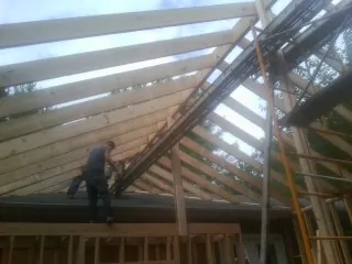 Rafters going up over a new addition with a worker on the wall in Baldwin