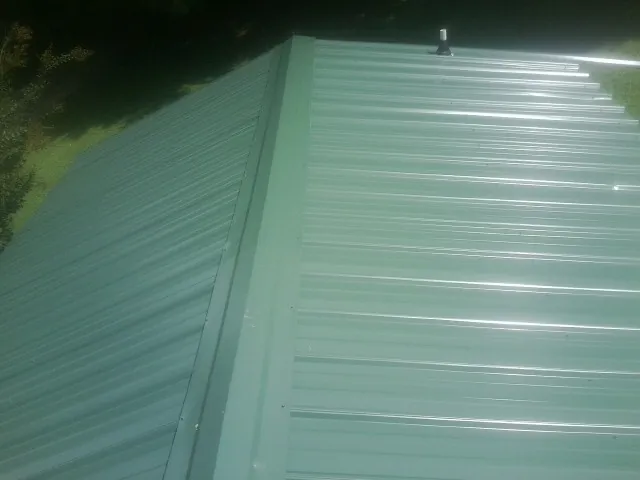 New green metal panels meeting at the ridge of a roof — Flat Roof Repair work by our crew in Baldwin