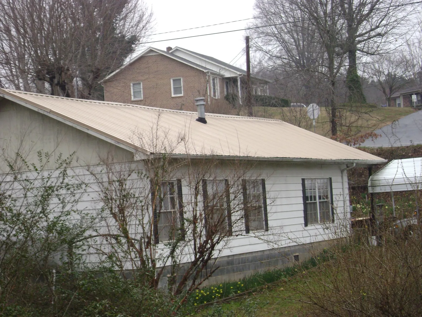 Tan metal roof on a white sided house set into a hillside — Commercial Roofing by Roofing Brothers in Baldwin